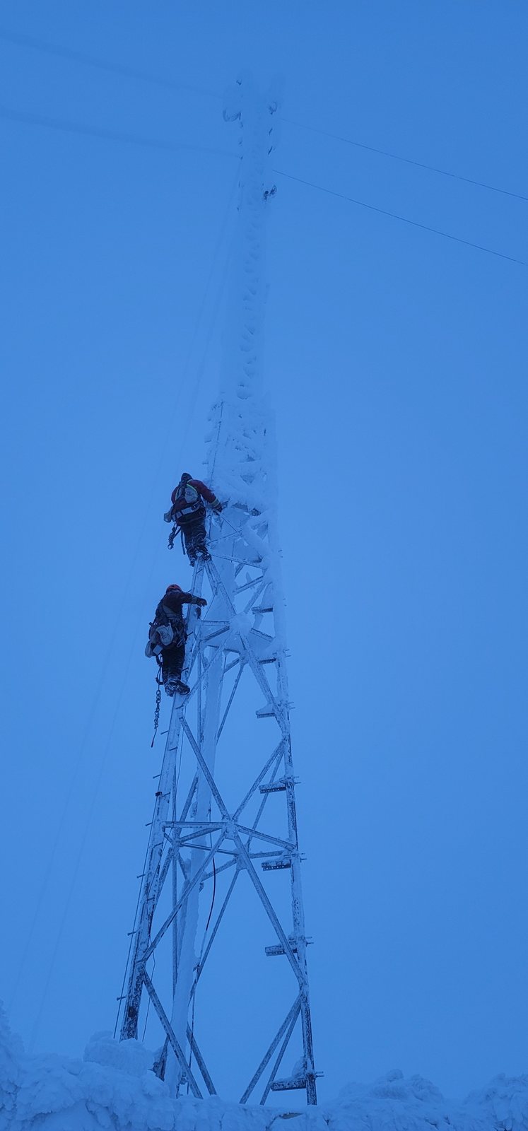 Two climbers ascending an ice-coated lattice tower
